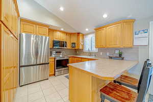 Kitchen with a breakfast bar, lofted ceiling, sink, appliances with stainless steel finishes, and kitchen peninsula