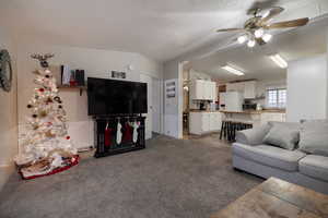 Living room with ceiling fan, dark carpet, lofted ceiling, and a textured ceiling