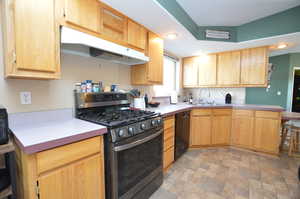 Kitchen with dishwasher, sink, stainless steel gas range, light brown cabinetry, and kitchen peninsula