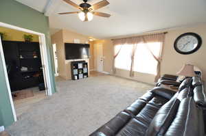 Carpeted living room with ceiling fan and lofted ceiling