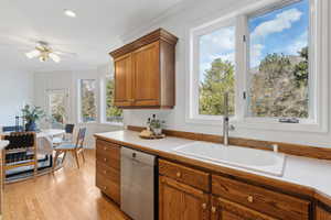 Kitchen with sink, light hardwood / wood-style flooring, stainless steel dishwasher, ceiling fan, large windows with views over the sink and walk out to deck