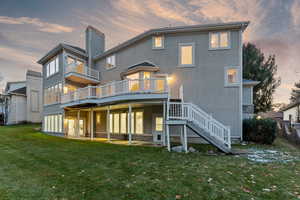 Back house at dusk featuring a wooden deck and a lawn