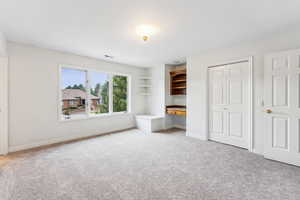 Freshly painted and carpeted bedroom with large windows, storage seat, built in shelves and desk