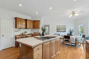 Kitchen featuring ceiling fan, crown molding, light hardwood / wood-style floors, stainless steel stovetop, and a center island with sink and walk out to deck