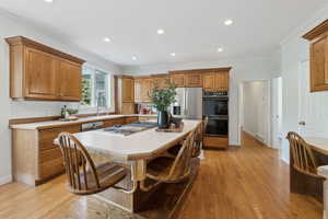 Kitchen with a center island, sink, crown molding, light wood-type flooring, and appliances with stainless steel finishes