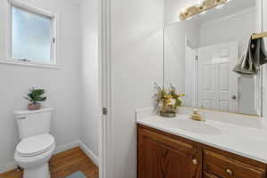 Main floor full bathroom with vanity, crown molding, bath / shower combo with glass door, hardwood / wood-style flooring, and toilet