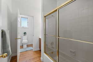 Main floor full bathroom with vanity, crown molding, bath / shower combo with glass door, hardwood / wood-style flooring, and toilet