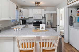 Kitchen featuring washer / clothes dryer, white cabinetry, sink, and appliances with stainless steel finishes