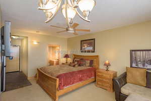 Bedroom featuring light carpet, a textured ceiling, and ceiling fan with notable chandelier