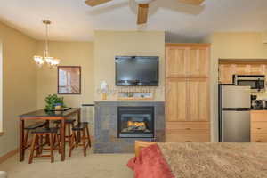 Kitchen with light brown cabinets, pendant lighting, light colored carpet, a tiled fireplace, and appliances with stainless steel finishes