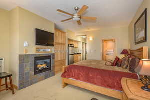 Bedroom with carpet flooring, a tiled fireplace, ceiling fan, and a textured ceiling