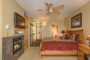 Bedroom featuring dark carpet, a tile fireplace, ceiling fan, a textured ceiling, and stainless steel refrigerator