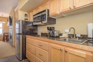 Kitchen featuring dark carpet, hanging light fixtures, sink, light brown cabinetry, and appliances with stainless steel finishes