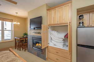 Kitchen featuring stainless steel fridge, light brown cabinetry, pendant lighting, a fireplace, and carpet floors