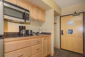 Kitchen with black electric stovetop, light brown cabinets, dark tile patterned floors, and sink