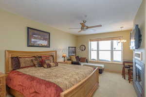 Bedroom with a textured ceiling, light colored carpet, and ceiling fan with notable chandelier