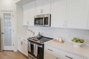 Picture is of model home. Kitchen featuring white cabinetry, backsplash, appliances with stainless steel finishes, and light hardwood / wood-style flooring