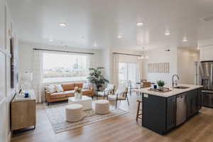 Picture is of model home. Kitchen with stainless steel appliances, a kitchen island with sink, decorative light fixtures, an inviting chandelier, and light hardwood / wood-style floors