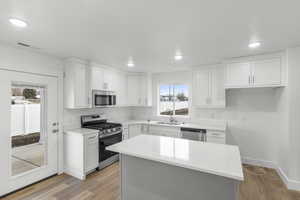 Kitchen with a center island, sink, stainless steel appliances, light hardwood / wood-style floors, and white cabinets