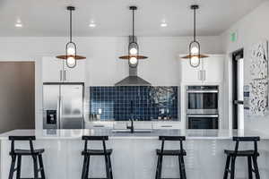 Kitchen with a kitchen breakfast bar, hanging light fixtures, appliances with stainless steel finishes, tasteful backsplash, and white cabinetry