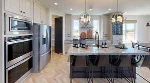 Kitchen with a large island, stainless steel appliances, light stone countertops, a notable chandelier, and decorative light fixtures