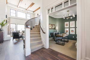 Stairs featuring an inviting chandelier, hardwood / wood-style floors, beam ceiling, and a towering ceiling