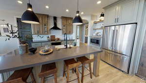 Kitchen featuring wall chimney exhaust hood, stainless steel appliances, sink, and an island with sink