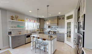 Kitchen featuring gray cabinets, a breakfast bar area, an island with sink, and appliances with stainless steel finishes