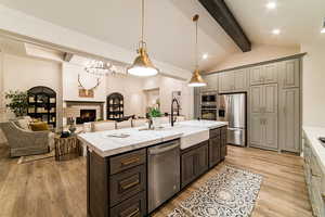 Kitchen featuring sink, appliances with stainless steel finishes, a kitchen island with sink, hanging light fixtures, and light stone countertops
