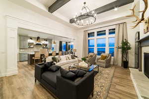 Living room with light hardwood / wood-style flooring, a chandelier, a water view, a fireplace, and beamed ceiling