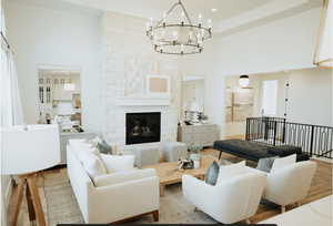 Living area featuring a high ceiling, wood finished floors, a stone fireplace, and a chandelier