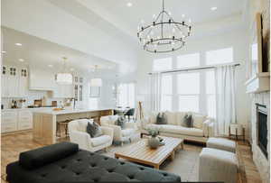 Living room featuring light wood-style floors, recessed lighting, a fireplace, a raised ceiling, and a chandelier