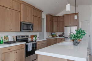 Kitchen with lofted ceiling, an island with sink, appliances with stainless steel finishes, and tasteful backsplash
