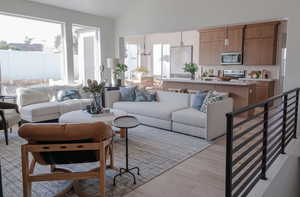 Living room featuring light wood-type flooring, vaulted ceiling, a chandelier, and plenty of natural light