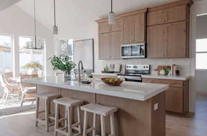 Kitchen with appliances with stainless steel finishes, an island with sink, decorative light fixtures, and backsplash