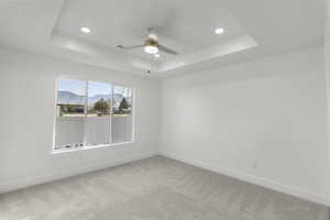 Carpeted empty room with a mountain view, ceiling fan, and a raised ceiling