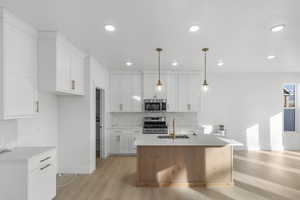 Kitchen featuring white cabinets, appliances with stainless steel finishes, a kitchen island with sink, and pendant lighting