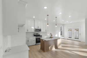 Kitchen featuring sink, hanging light fixtures, a center island with sink, white cabinets, and appliances with stainless steel finishes