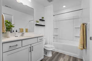 Full bathroom with wood-type flooring, vanity, toilet, and shower / bathtub combination with curtain