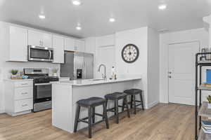 Kitchen featuring kitchen peninsula, light hardwood / wood-style flooring, appliances with stainless steel finishes, a kitchen bar, and white cabinetry