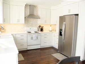 Kitchen with dark wood-type flooring, wall chimney range hood, sink, electric stove, and stainless steel fridge