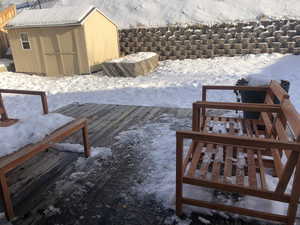 Yard layered in snow featuring a deck and a storage shed