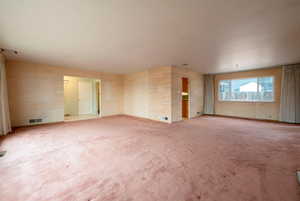 Living room connected to dining room with large windows and hardwood floors under carptet