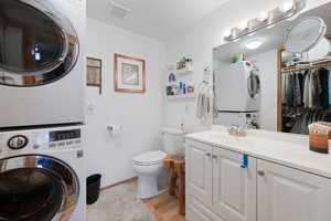 Bathroom with vanity, toilet, wood-type flooring, and stacked washer and dryer