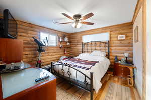 Bedroom featuring rustic walls, light hardwood / wood-style flooring, and ceiling fan