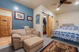 Bedroom with light hardwood / wood-style flooring, ceiling fan, a barn door, a spacious closet, and a closet