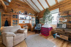 Living room featuring beamed ceiling, light hardwood / wood-style floors, rustic walls, and high vaulted ceiling