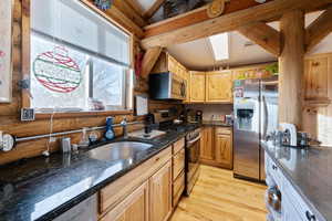 Kitchen with dark stone counters, stainless steel appliances, sink, light hardwood / wood-style flooring, and beamed ceiling