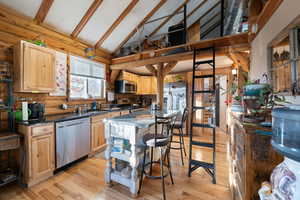 Kitchen with light brown cabinets, high vaulted ceiling, light wood-type flooring, appliances with stainless steel finishes, and beam ceiling