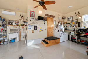 Garage with a wall mounted air conditioner, a workshop area, white refrigerator, and ceiling fan